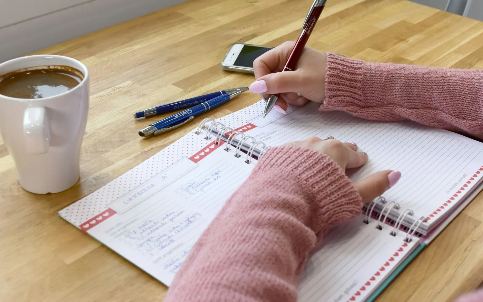 Person writing in a journal at a wooden table next to a cup of coffee
