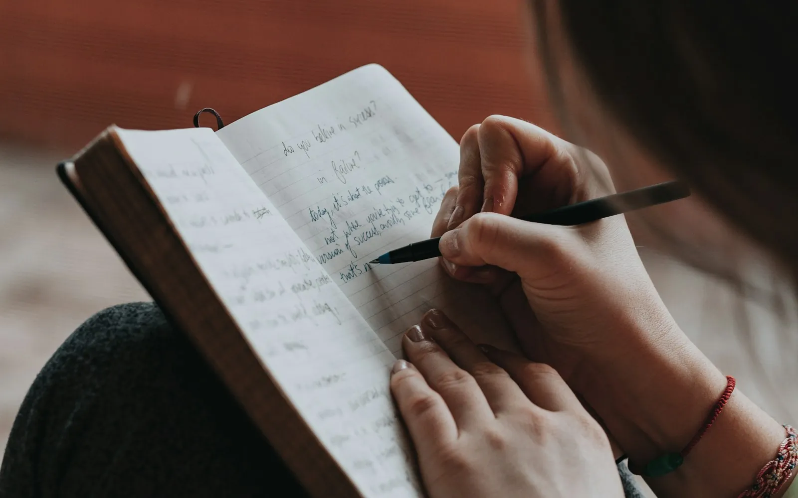 Woman writing by hand in a small gratitude journal